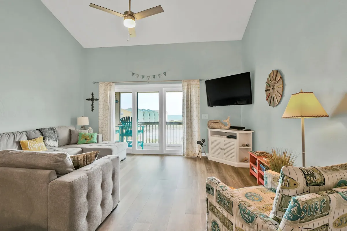 A cozy interior living space with a comfortable sofa facing glass doors that open to an outside view, allowing natural light to stream in. The scene suggests a perfect spot for morning coffee, with the ocean visible beyond the balcony.