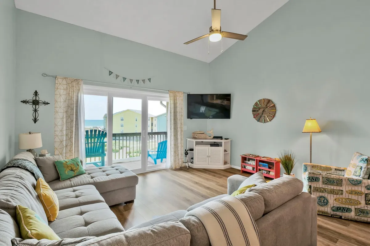 A spacious living room with a large sectional sofa, colorful accent chairs, a TV unit, and sliding glass doors that let in plenty of natural light. The décor is cozy and inviting, creating an ideal setting for movie nights or quiet family chats. The open vaulted ceiling hints at the connection to the upstairs loft space.