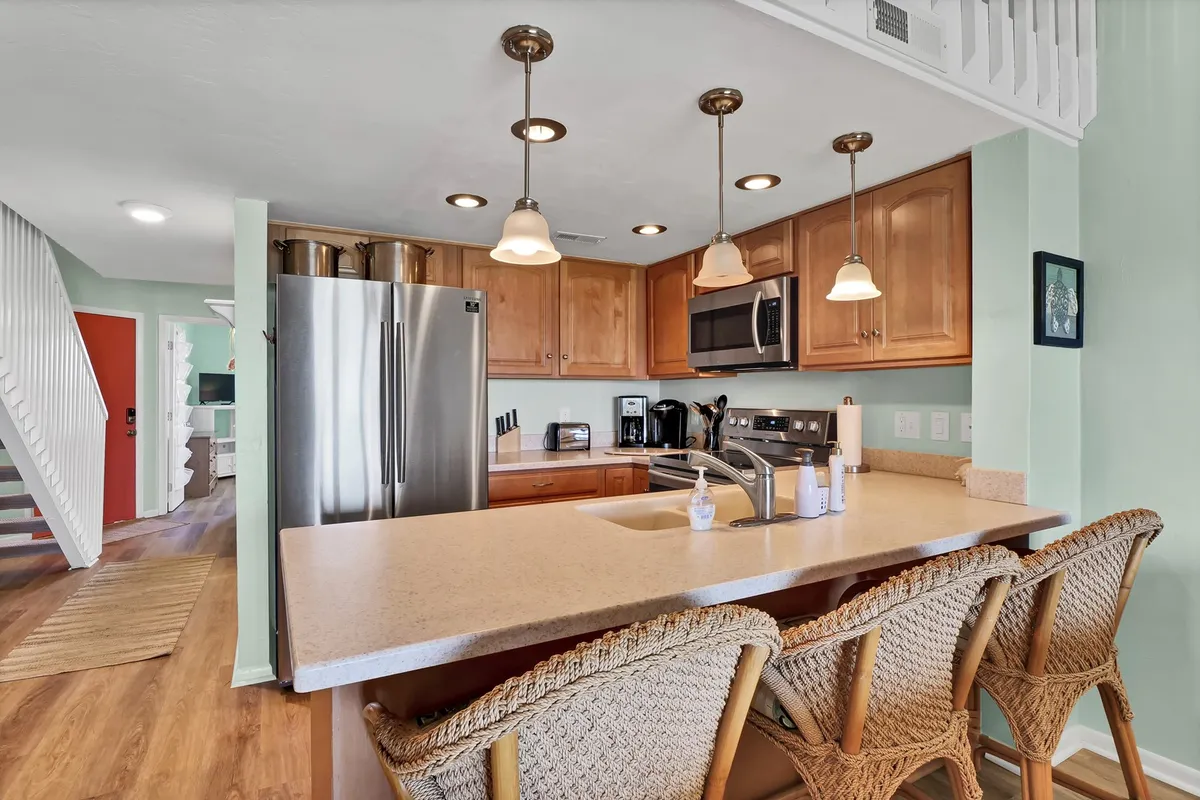 This image features a welcoming kitchen space with a granite-topped island, stainless steel appliances, and bar stools. The area is styled to evoke a sense of warmth, making it ideal for both casual breakfasts and evening gatherings. A glimpse of the open-concept design is visible, with the kitchen leading into the adjacent living and dining areas.