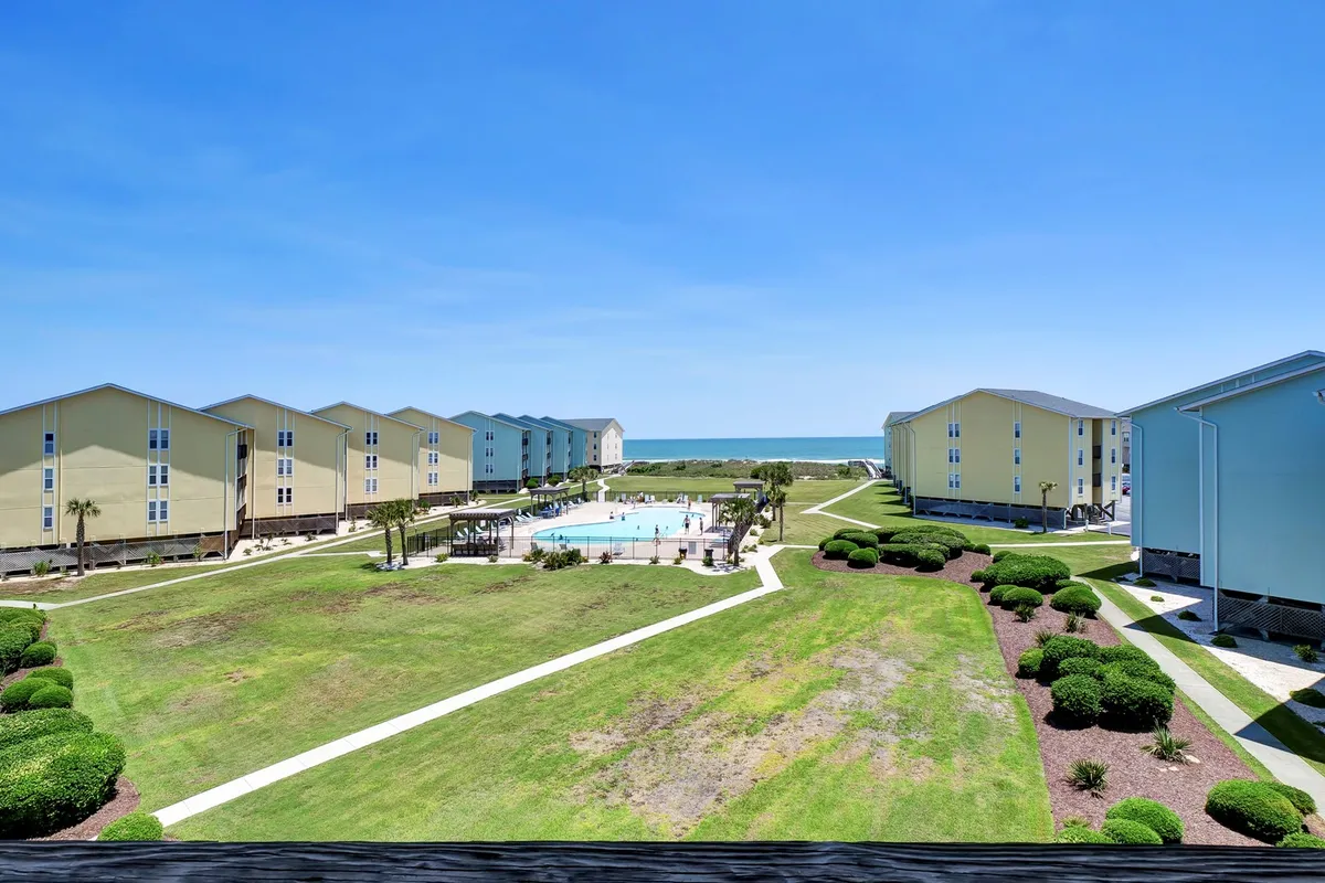 A relaxing, landscaped garden area bordering the swimming pool, with unobstructed beach views, community buildings, and areas for sunbathing and socializing. The image highlights both the communal pool and adjacent garden spaces designed for relaxation and gathering.
